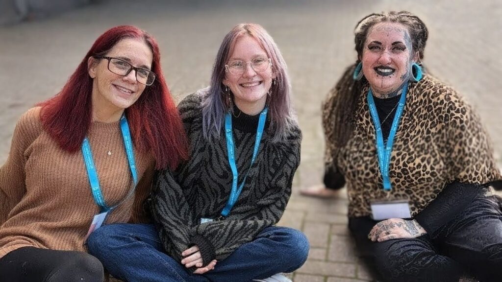 Image shows LLL Leaders Lisa, Nico and Jess sitting on the floor wearing LLL lanyards and smiling